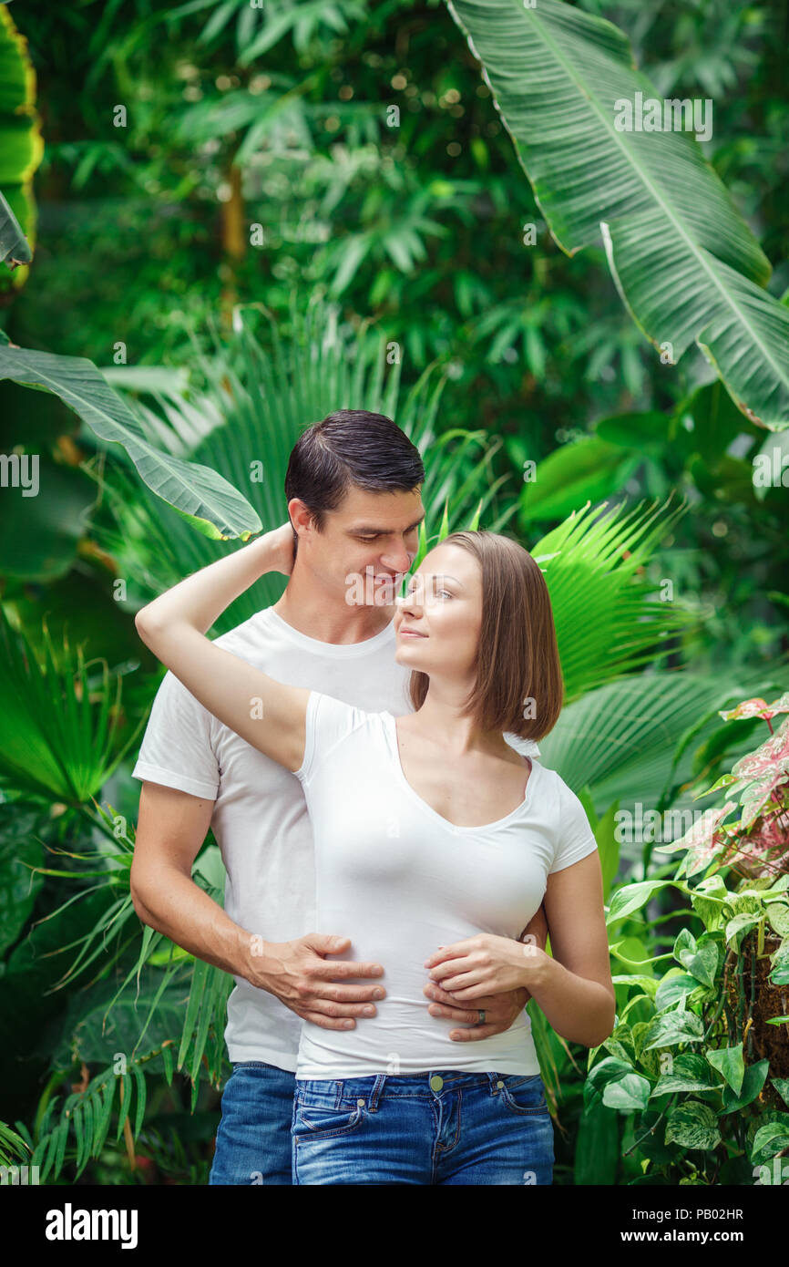 Portrait von zwei Menschen, Mann Frau Mädchen zusammen, unter grünen Bäumen, Pflanzen im Park außerhalb, Lächeln, Lachen, umarmen, wegsehen, intime m Stockfoto