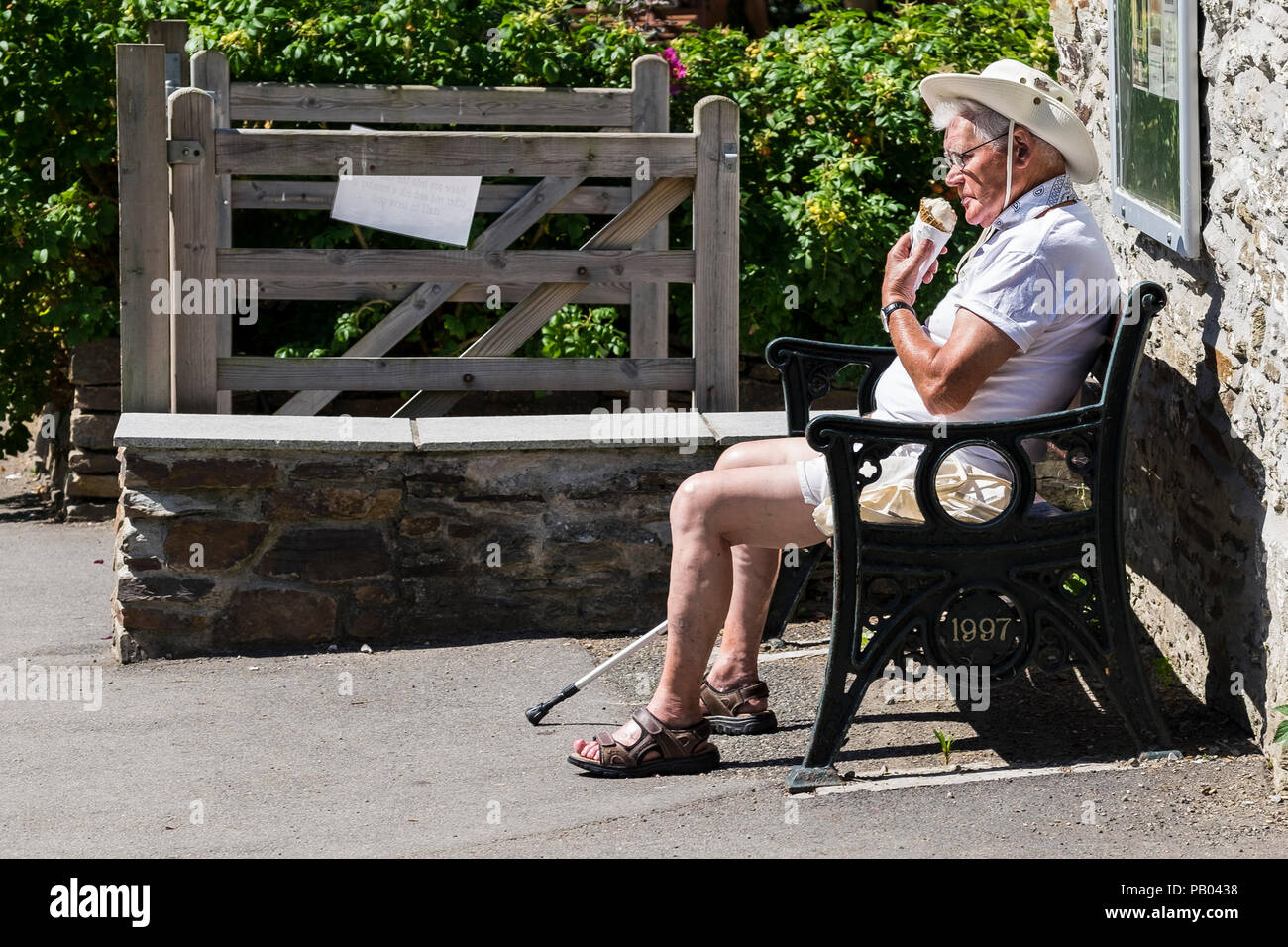 Ein reifer Urlauber, der in Weiß gekleidet ist und die Sonne und ein Eis in Newquay Cornwall genießt. Stockfoto