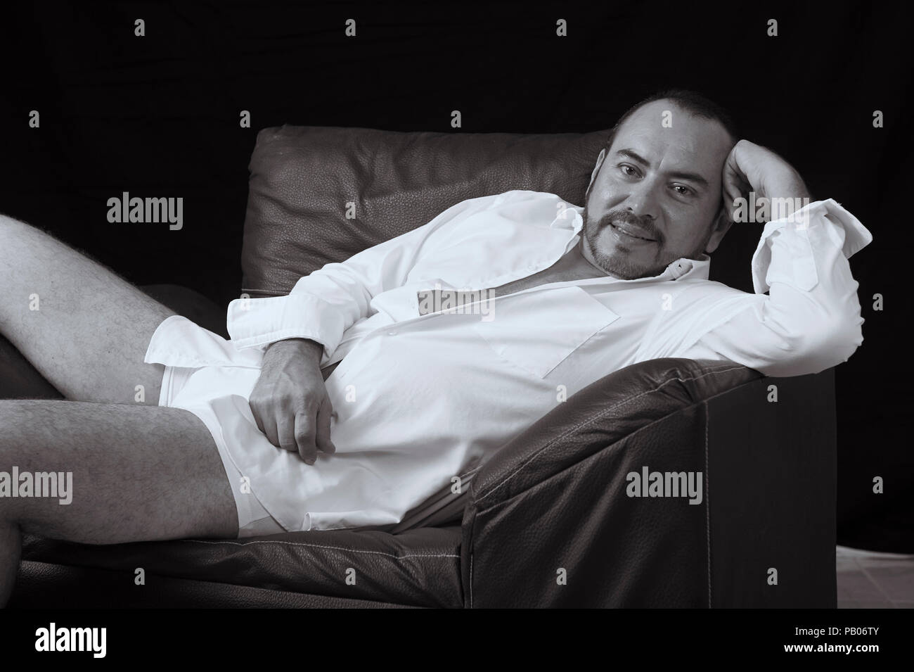 Schwarze und Weiße studio Porträt eines Mannes im weissen Hemd und Slip, liegend auf einem Sofa Stockfoto