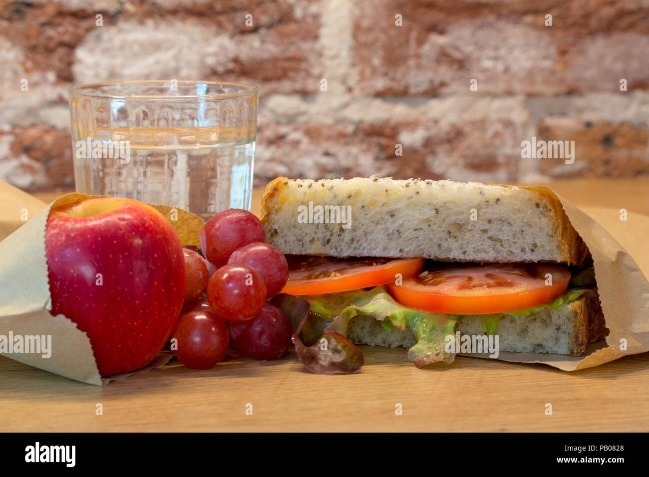Kunststoff kostenlos gesundes Mittagessen mit authentischen echte hausgemachte Speisen. Tomato Sandwich, Trauben, Apple und Glas Wasser. Stockfoto