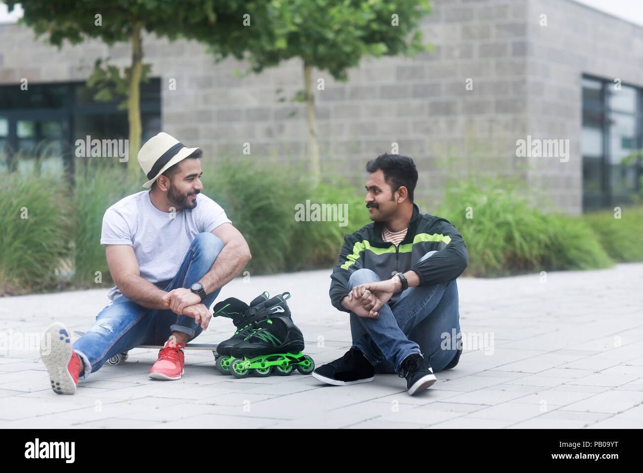 Zwei Männer sitzen im Freien mit einem Skateboard und Rollerblades Stockfoto