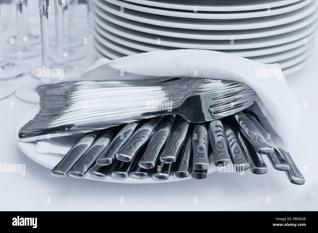 Elegantes Set von Gabeln und Messer Besteck mit Serviette auf weißen Tischdecke mit Haufen von Teller und Gläser Stockfoto