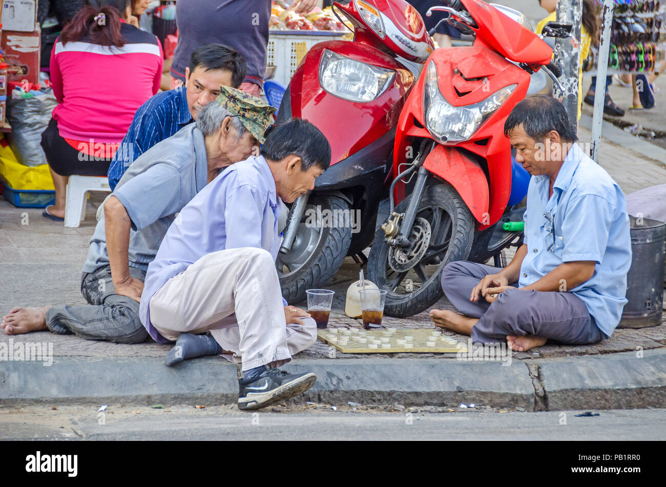 Ho Chi Minh City, Vietnam - 4. April 2018: Street Scene - Männer spielen traditionelle Brettspiel auf der Kreuzung in der Innenstadt zwischen geparkten Mopeds Stockfoto