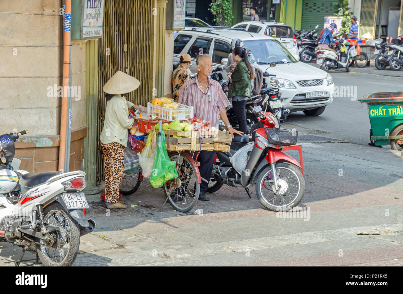Ho Chi Minh City, Vietnam - 4. April 2018: Street Scene - traditionelle Verkäuferin mit Ihrem Fahrrad voll mit Gemüse geladen, Moped Fahrer und pedestri Stockfoto