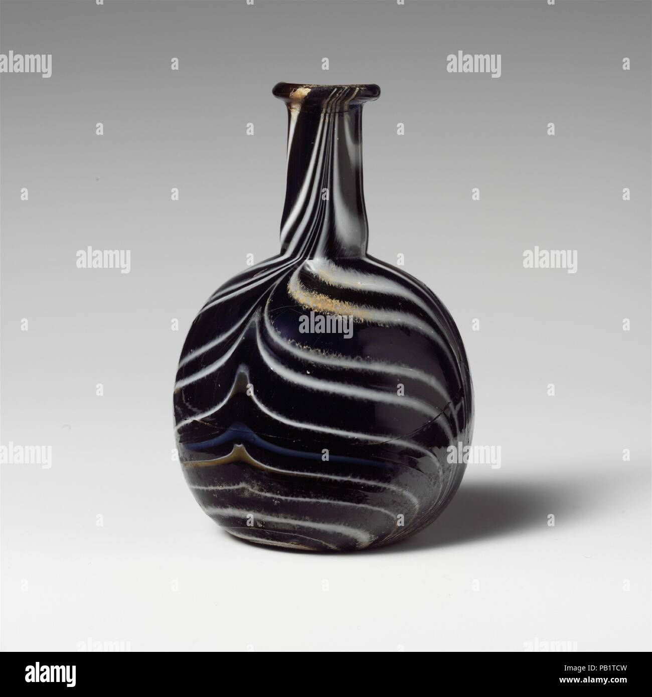 Glas Mosaik Parfüm Flasche. Kultur: Roman. Abmessungen: Durchm.: 4. (10,2 cm). Datum: 1. Halbjahr 1. Jh. N.CHR.. Transluzente tiefe Kobaltblau, mit durchscheinenden Honig braun, opak Weiße, opake Hellblau und opak Gelb Trails. Auch abgerundete, Rim, zylindrische Hals, leicht nach unten erweitert, mit feinen Gedankenstrich um Base; kugelförmigen Körper; konkave Unterseite. Gestreifte Mosaik Muster der angewandten Wanderwege rund auf blauem Grund gewickelt und dann nachgerüstet in vier Anschläge, abwechselnd nach oben und unten, in einen breiten Feder Muster. Gebrochen und repariert, mit einem großen Chip in Rim, und eine Bohrung ein Stockfoto