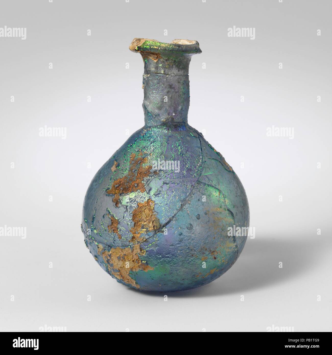 Glas Parfüm Flasche. Kultur: Roman. Abmessungen: 3 1/8 in. (7,9 cm) Durchmesser: 2 1/4 in. x 7/8 in. (5,7 x 2,2 cm). Datum: 1. Jh. N.CHR.. Transluzent blau. Schiefe rim ausgeklappt, über und mit vertikalen innere Lippe; zylindrische Hals, mit schnittspuren um Base; breite piriform Körper; flachen Boden. Rad-cut horizontale Nut um den Oberkörper. Gebrochen und repariert, mit zahlreichen Löchern und Verluste, und viele Risse; Nadelstich und größere Blasen; Mattierung, tiefe Rillen, und brillante irisierende Verwitterung. Dicke, schwere Glas. Museum: Metropolitan Museum of Art, New York, USA. Stockfoto