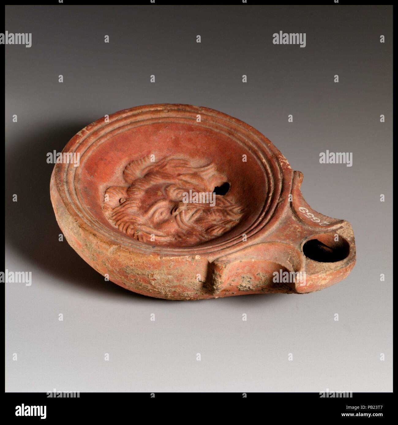 Terrakotta Öllampe. Kultur: Roman, der Zyprischen. Abmessungen: Insgesamt: 1 1/4 x 4 in. (3,2 x 10,2 cm). Datum: 1. Jahrhundert v. Chr. - 1. nachchristlichen Jahrhundert. Loeschcke Typ 1 A. Schimmel gebildet. Discus: Leiter des Silen, mit Bart, spitzen Ohren und Hörner. Single Einfüllöffnung am unteren rechten, mit einer Band von Linien und Rillen auf Kante. Voluten flankierende eckig Düse. Angehobene base Ring und flache Unterseite. Komplette, außer für großes Loch in der Grundplatte und Finial der Spirale auf der rechten Seite. Museum: Metropolitan Museum of Art, New York, USA. Stockfoto