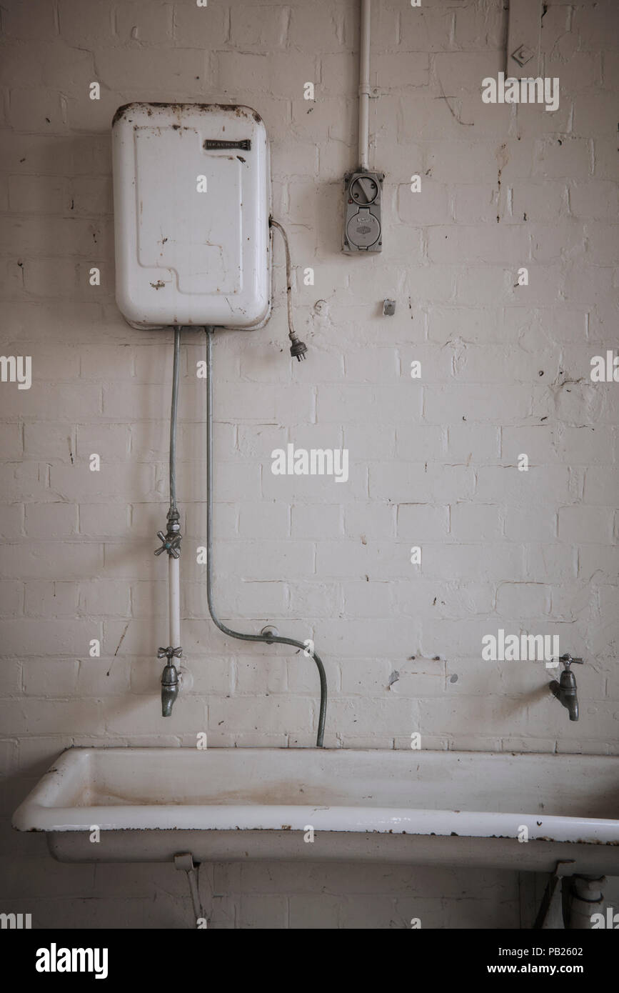 Alten, verlassenen heißes Wasser Service über ein großes, weißes Porzellan Waschbecken in einem weißen Stein Zimmer. Stockfoto