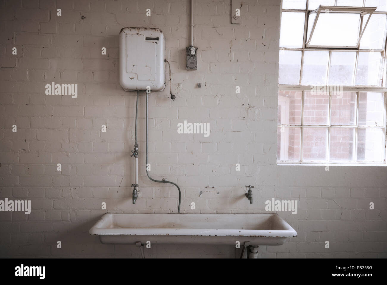 Alten, verlassenen heißes Wasser Service über ein großes, weißes Porzellan Waschbecken in einem weißen Stein Zimmer. Stockfoto
