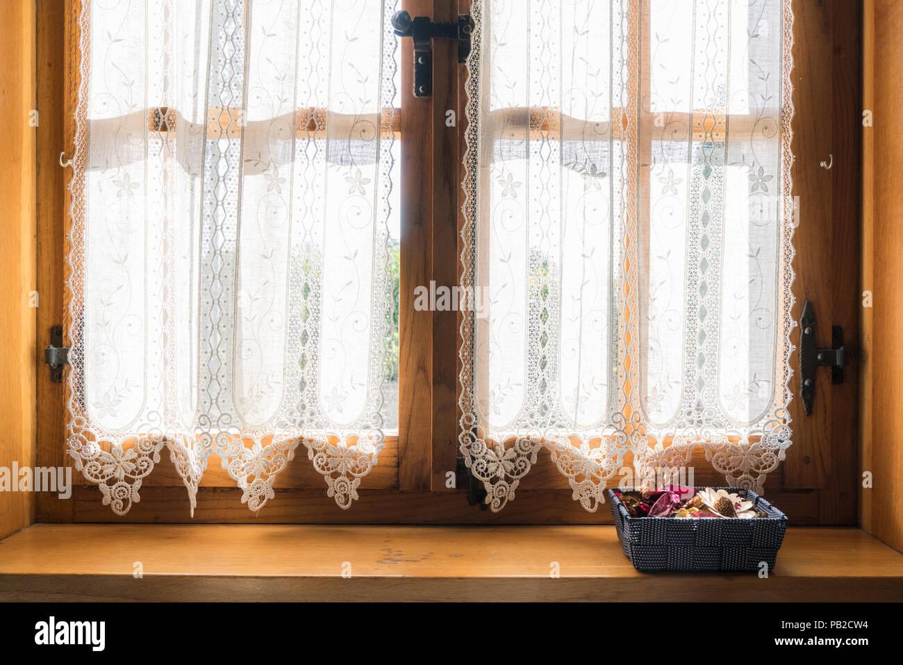 Eine Holz- Fenster mit einem weißen bestickten Vorhang und einen kleinen Korb mit getrockneten Blumen auf der Fensterbank Stockfoto