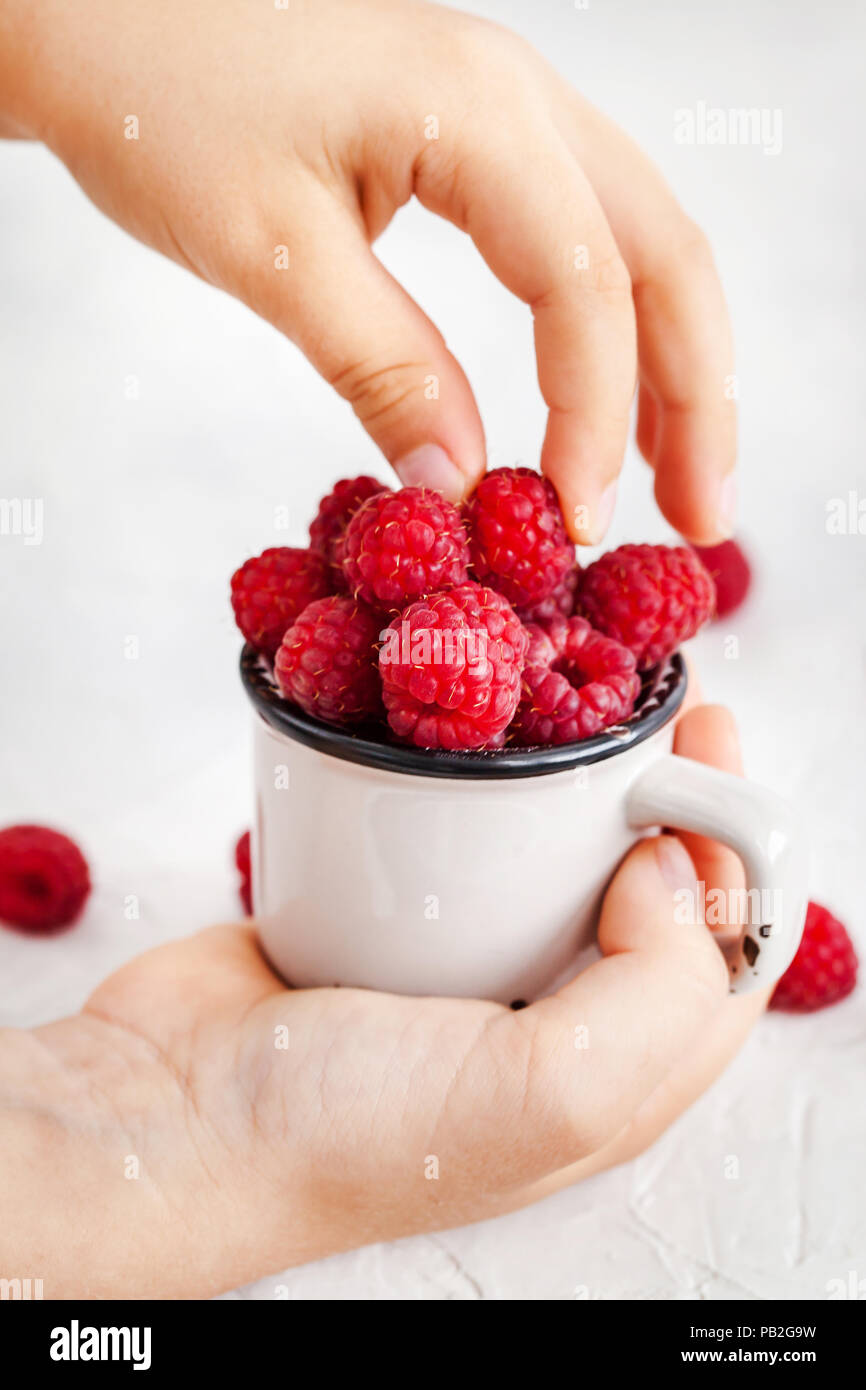 Frische reife Himbeeren in Becher in die Hände von Kindern Stockfoto