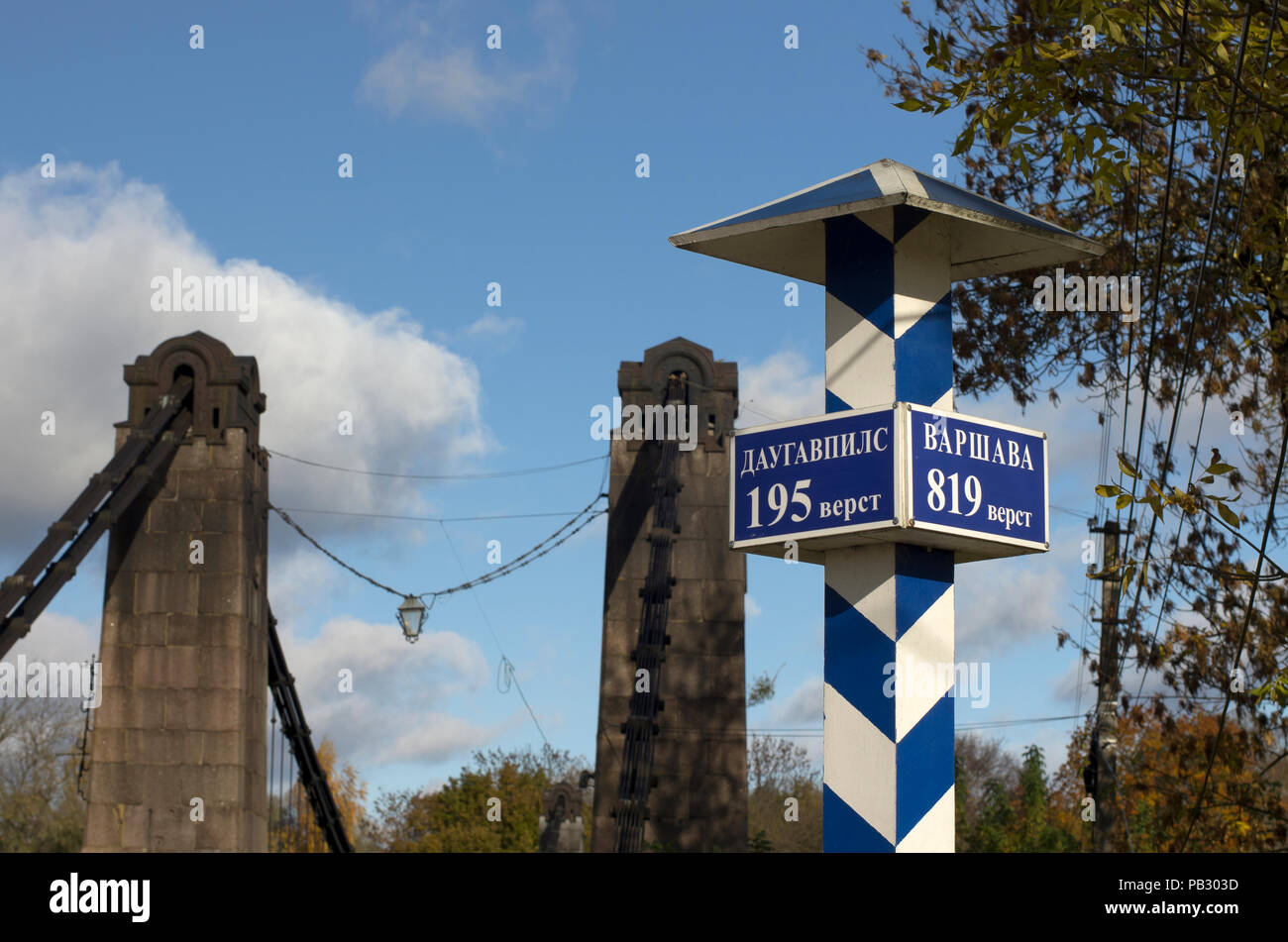 Milepost mit Namen der Städte in der Russischen und der Entfernung in Kilometern und mit der Suspension Bridge auf einem Hintergrund Stockfoto