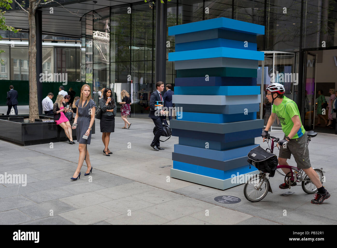 Ein Blick zwischen einer jungen Frau und einem Radfahrer Vor dem Kunstwerk berechtigt Stack Blues von Sean Scully RA, am 25. Juli 2018, in der Londoner City. Teil von Scully's Festnetz Serie von Arbeiten, Stack Blues ist eine Skulptur aus der Auseinandersetzung des Künstlers mit dem Horizont getragen. Stockfoto