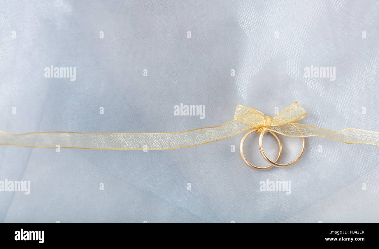 Ein paar goldene Hochzeit Ringe mit einem goldenen Band auf silber glänzenden Hintergrund gebunden, kopieren Raum Stockfoto