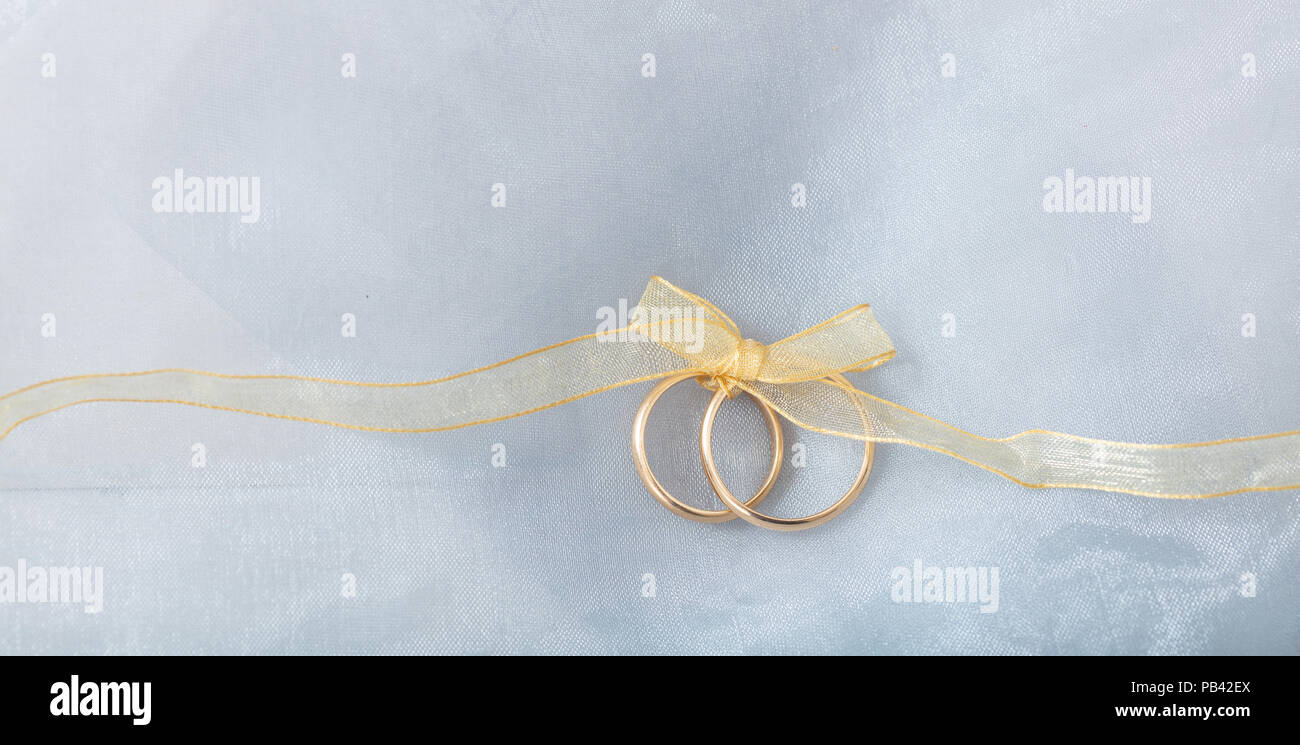 Ein paar goldene Hochzeit Ringe mit einem goldenen Band auf silber glänzenden Hintergrund gebunden, kopieren Raum Stockfoto