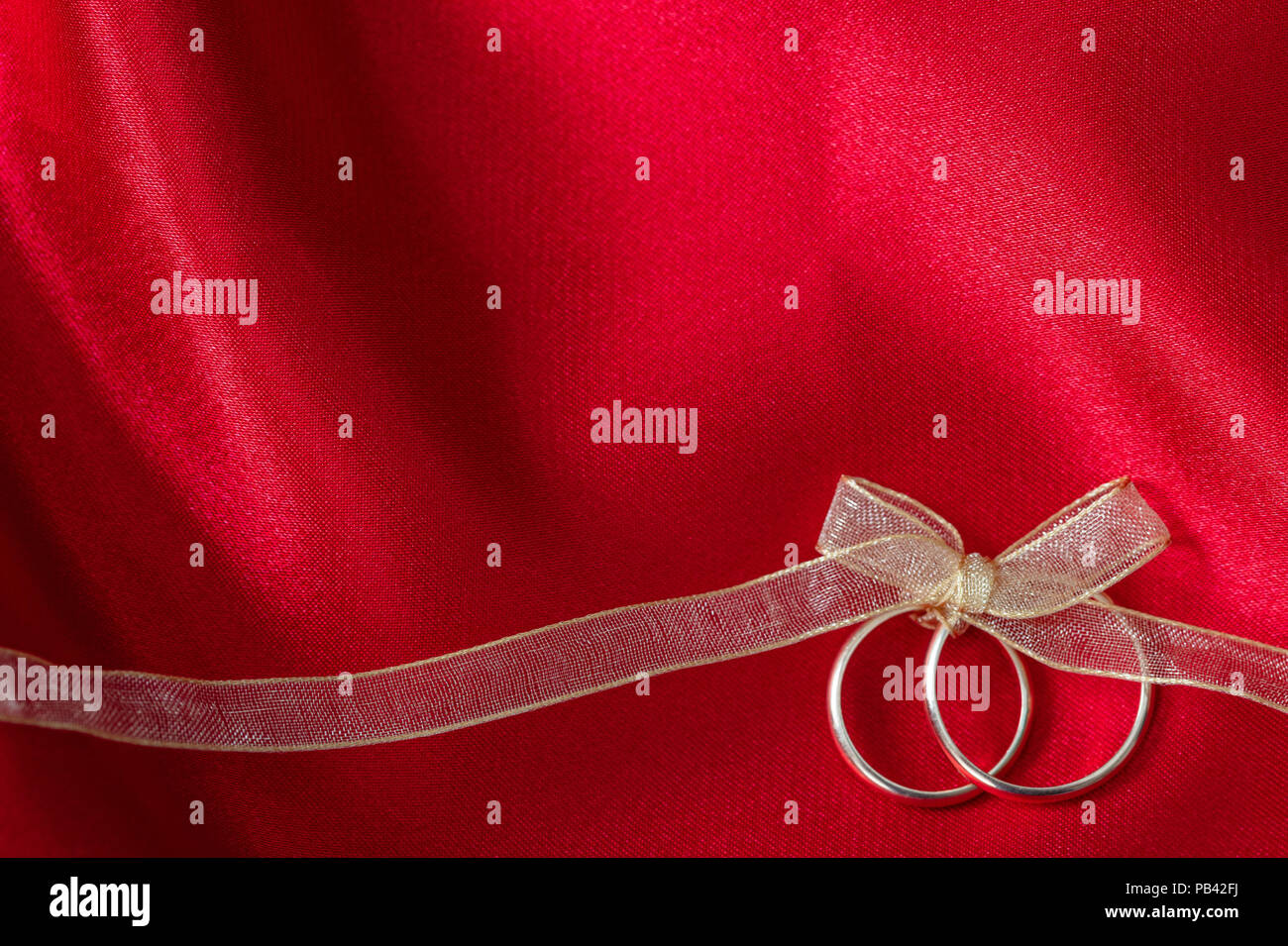 Ein paar goldene Hochzeit Ringe mit einem goldenen Band auf rotem Satin Hintergrund gebunden, kopieren Raum Stockfoto