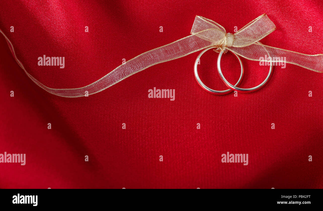 Ein paar goldene Hochzeit Ringe mit einem goldenen Band auf rotem Satin Hintergrund gebunden, kopieren Raum Stockfoto