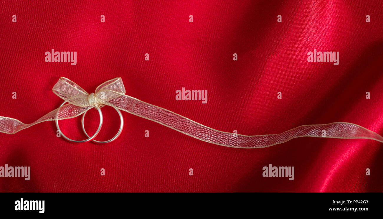 Ein paar goldene Hochzeit Ringe mit einem goldenen Band auf rotem Satin Hintergrund gebunden, kopieren Raum Stockfoto