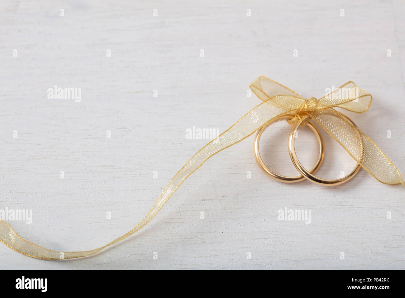 Ein paar goldene Hochzeit Ringe mit einem goldenen Band auf weißen Hintergrund Holz gebunden, kopieren Raum Stockfoto