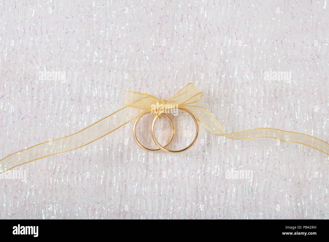 Ein paar goldene Hochzeit Ringe mit einem goldenen Band auf weiß leuchtendem Hintergrund gebunden, kopieren Raum Stockfoto