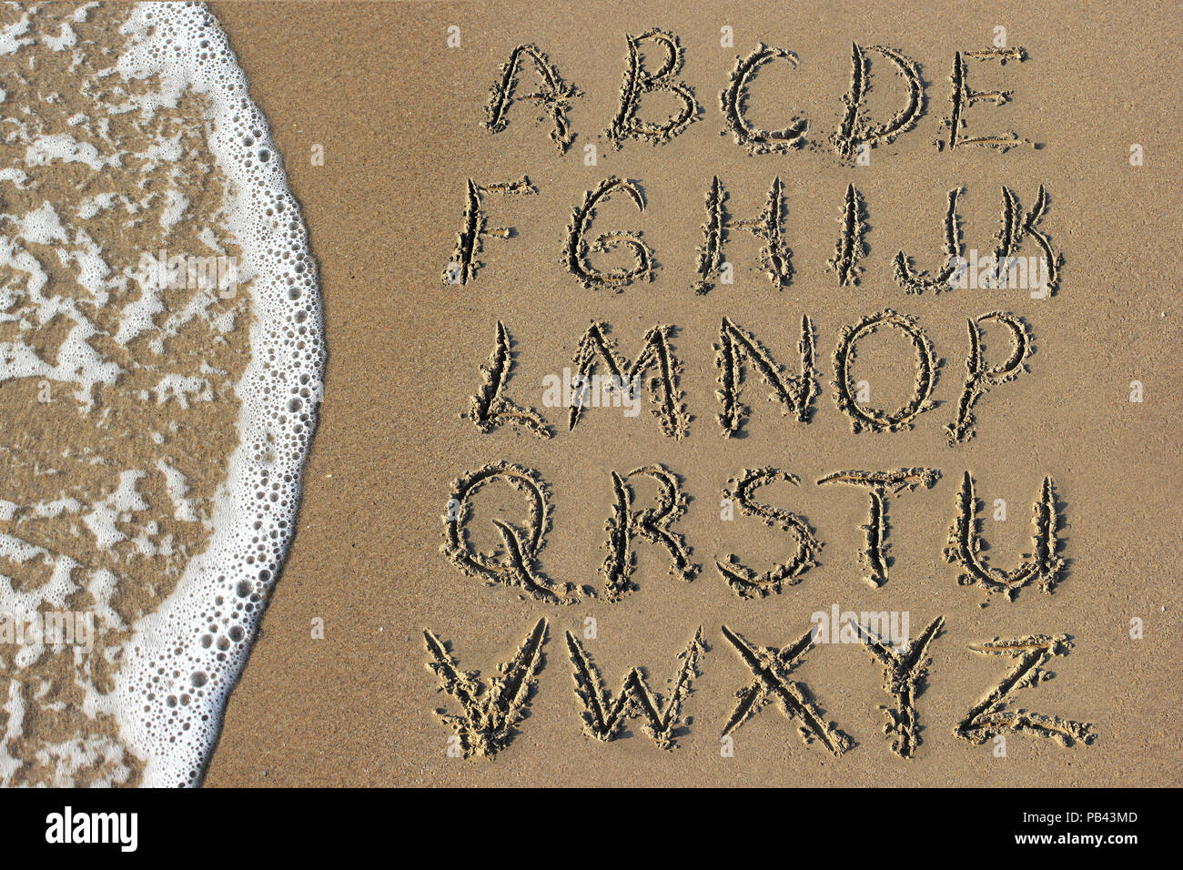 Buchstaben des Alphabets handschriftlich in Sand am Strand Stockfoto