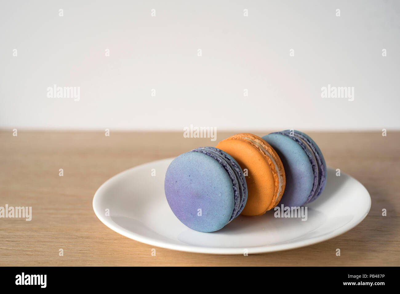 3 Orange und Blau Macarons sitzen auf ihren Seiten auf einer Platte Stockfoto