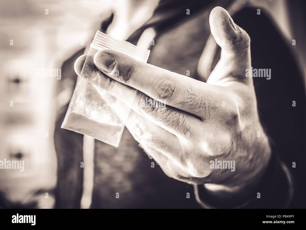 Behandlung illegaler Drogen von einem Mann mit einem kleinen Beutel mit weißem Pulver in seine Hand in monochromen Farben Stockfoto