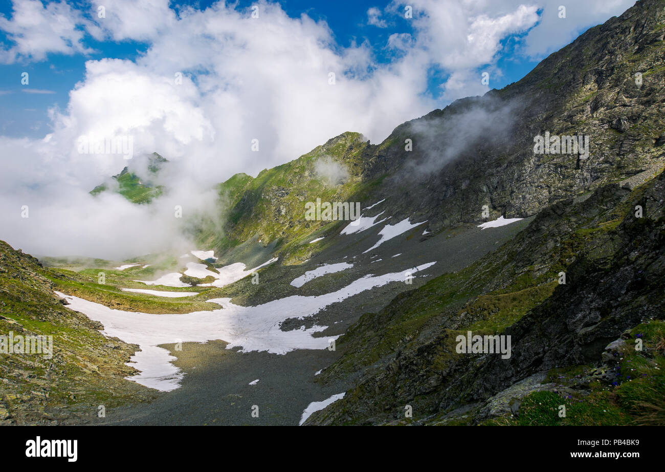 Flecken Schnee im Tal mit felsigen Klippen. entfernten Berg in der Wolkenbildung. wunderschöne Sommer Landschaft auf einer Höhe Stockfoto