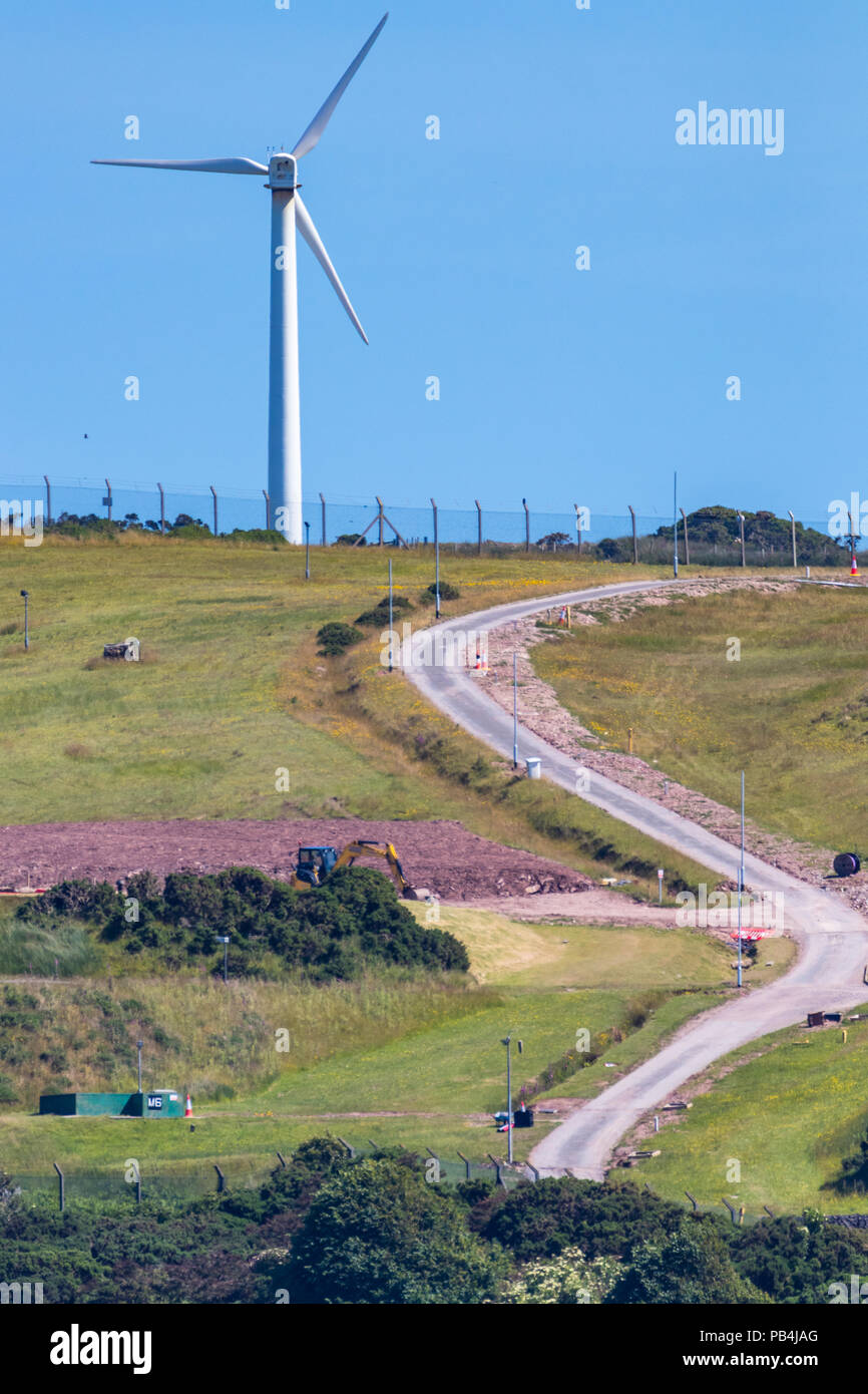 Vertikale Foto von einer einzelnen Windenergieanlage auf einem grünen Hügel mit einem gewundenen Straße und einem blauen Himmel. Stockfoto