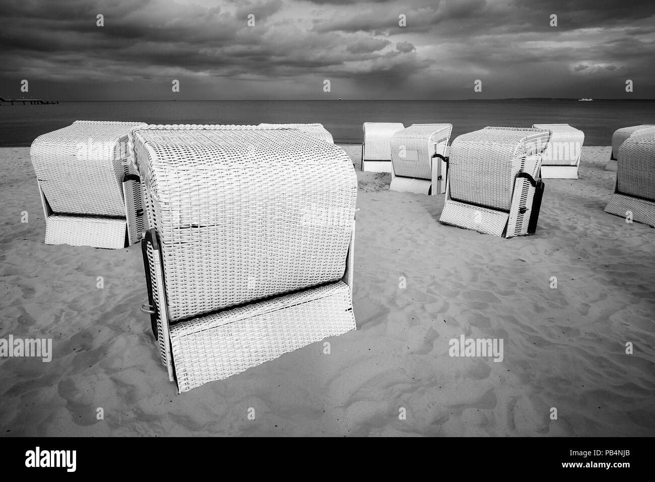 Hooded Weidenkorb Stühle auf einen leeren Strand vor einem Sturm. Stockfoto