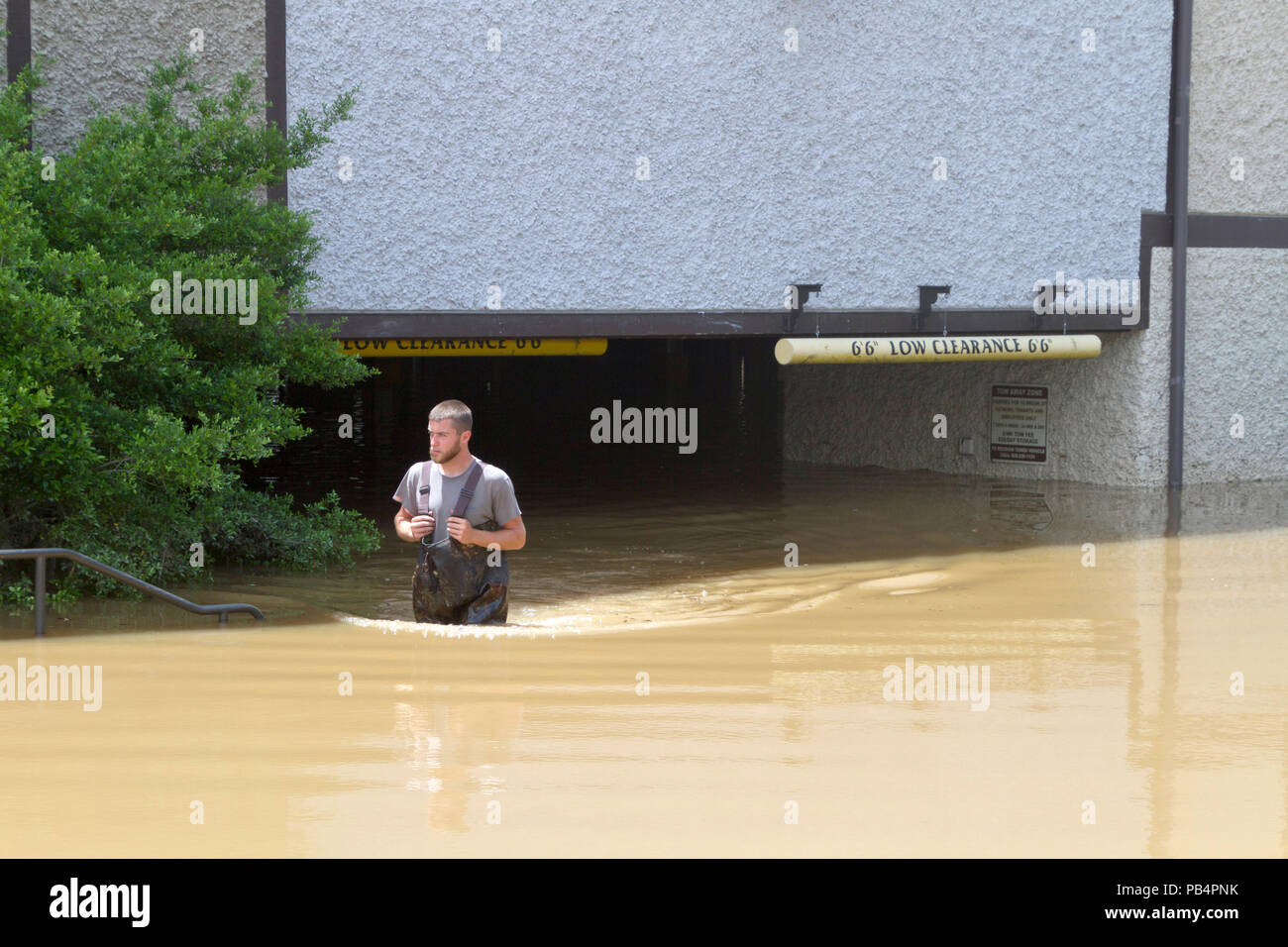 ASHEVILLE, North Carolina, USA - Mai 30, 2018: Ein junger Mann watet durch Hip hohe schlammiges Wasser, während er sich von einem überfluteten niedrige Ebene Parkplatz Garage Stockfoto