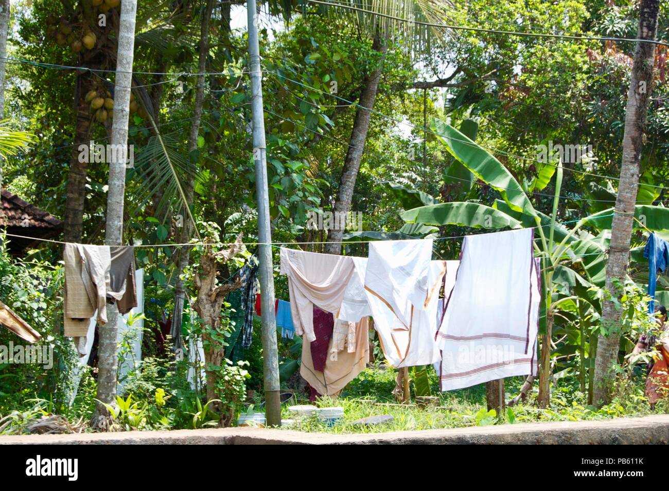 Wäscheleine mit frisch gewaschene bunte traditionelle indische Kleidung in den Wind hängen an einem sonnigen Sommertag in der Landschaft von ländlichen Kerala Stockfoto