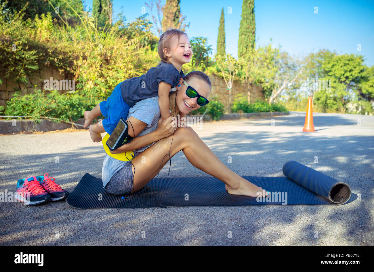 Gesunde Familie leben, nette Fröhliche baby boy spielt Huckepack und hilft ihr zu tun Stretching, schöne Frau mit ihrem kleinen Sohn Sport excercise Stockfoto