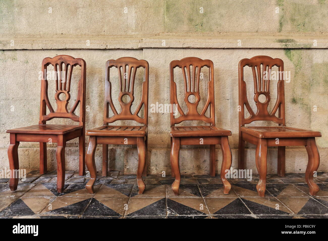 Set mit 4 von Hand aus Holz geschnitzte Stühle mit Rückenlehne - klassisches Design poliert und auf der gefliesten Boden lackiert - Coral Steinmauer. Santa Monica Pfarrei Stockfoto