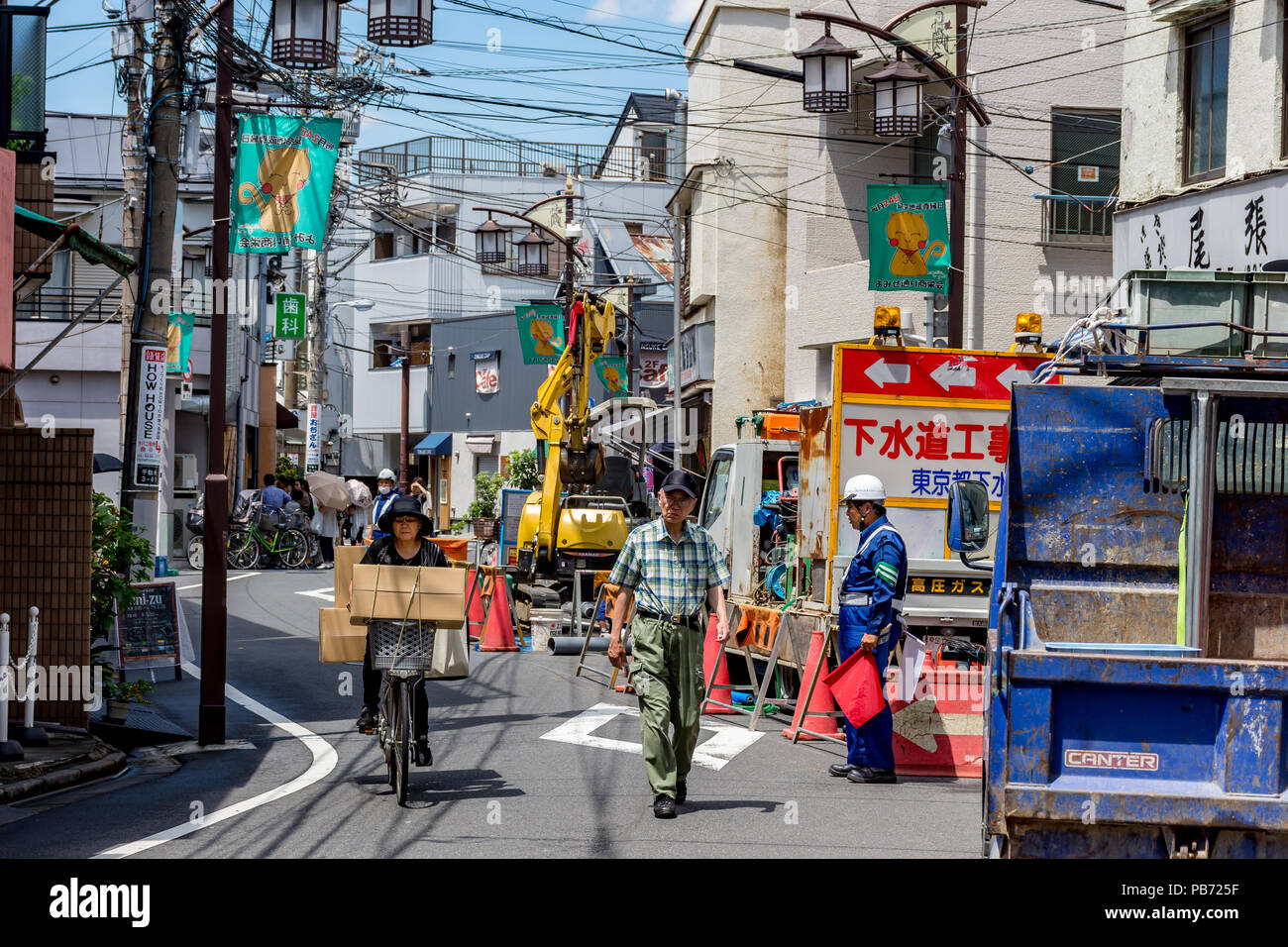 Frau auf Fahrrad mit großen Boxen Zyklen vorbei an alten Menschen vorbeigehen Straße Baustelle mit Hut mit roten Fahnen, in Tokio, Japan. Stockfoto