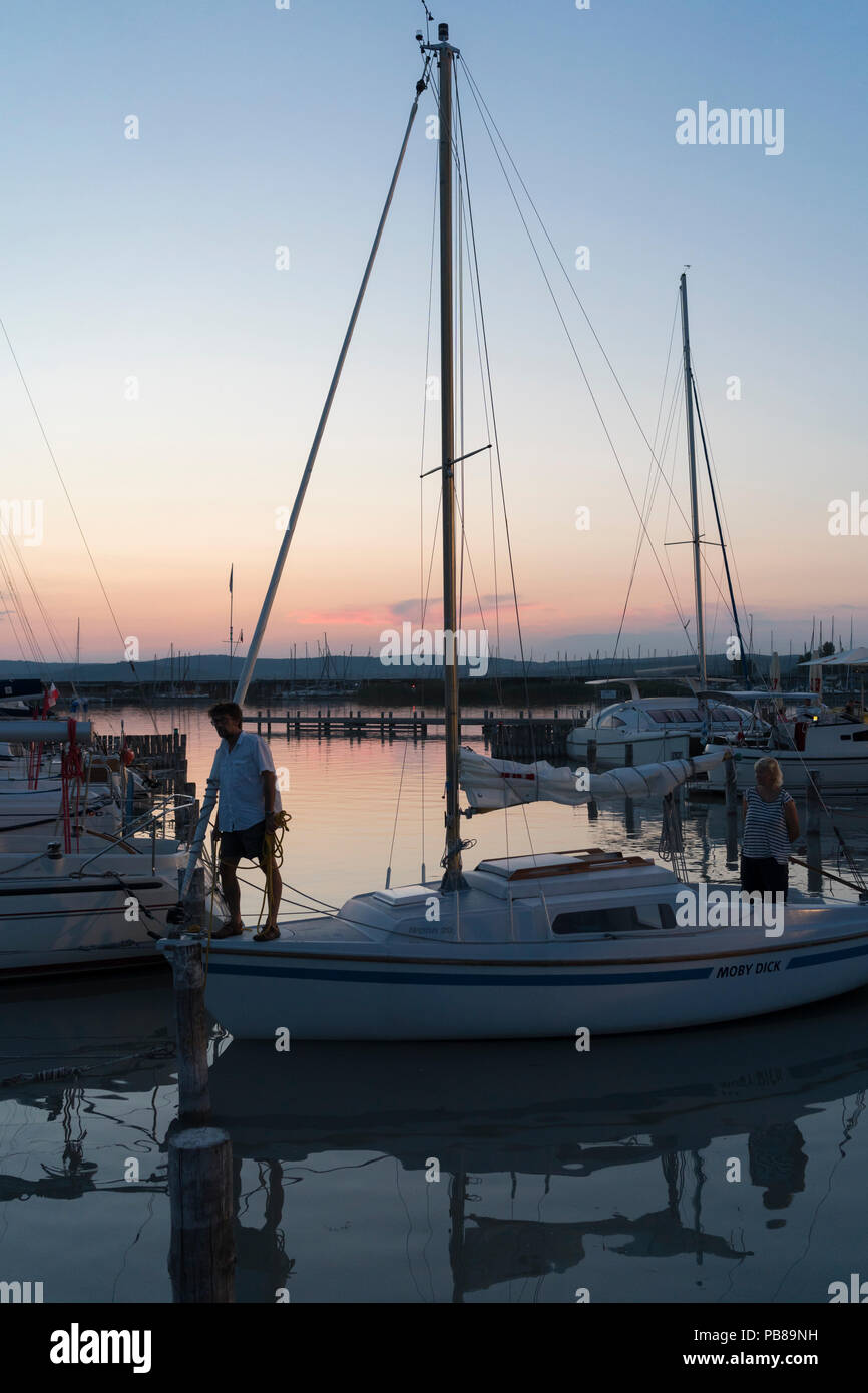 Ein Mann auf einem Segelboot vorbereiten, in der Dämmerung in einer Sommernacht am Neusiedler See zu binden am See, Burgenland Stockfoto