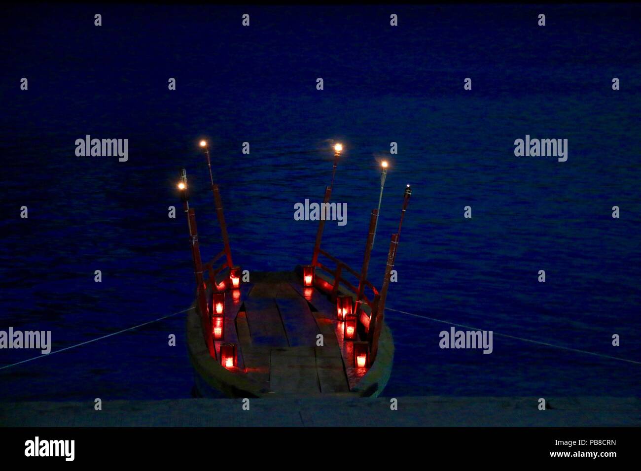 Kerzen und Fackeln beleuchtet kleines Holzboot auf einem See Stockfoto