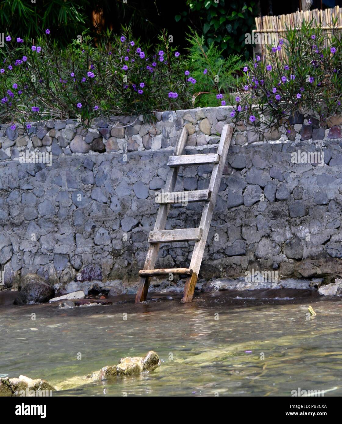 Holzleiter lehnte sich gegen eine Wand an einem See. Stockfoto