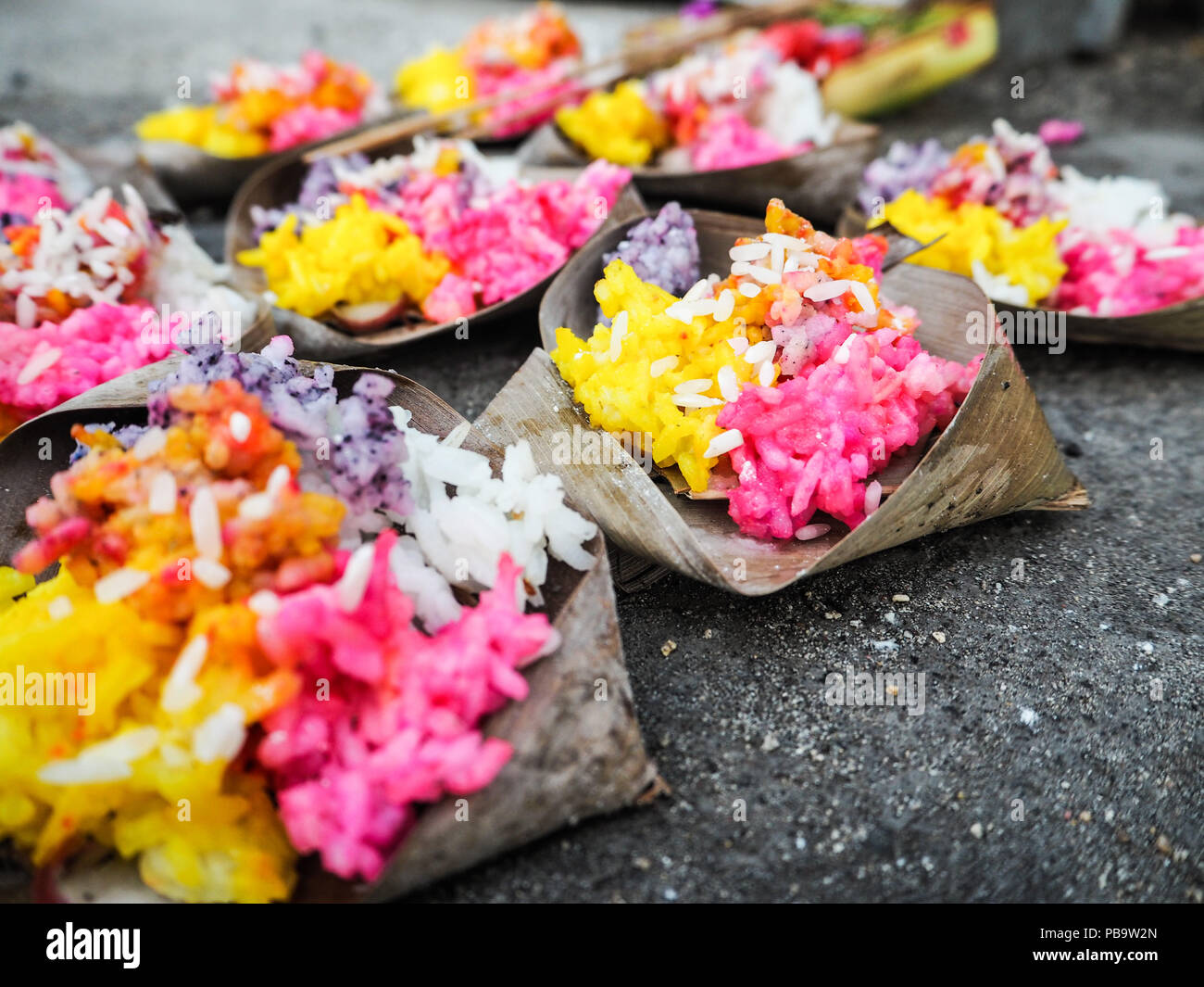 Reihen von hellen Gelb und Rosa Reis Angebote in der Palme treibt auf dem Bürgersteig an Saka Silvester während Nyepi, Nusa Lembongan, Bali, Indonesien Stockfoto Reihen von hellen Gelb und Rosa Reis Angebote in der Palme treibt auf dem Bürgersteig an Saka Silvester während Nyepi, Nusa Lembongan, Bali, Indonesien Stockfoto
