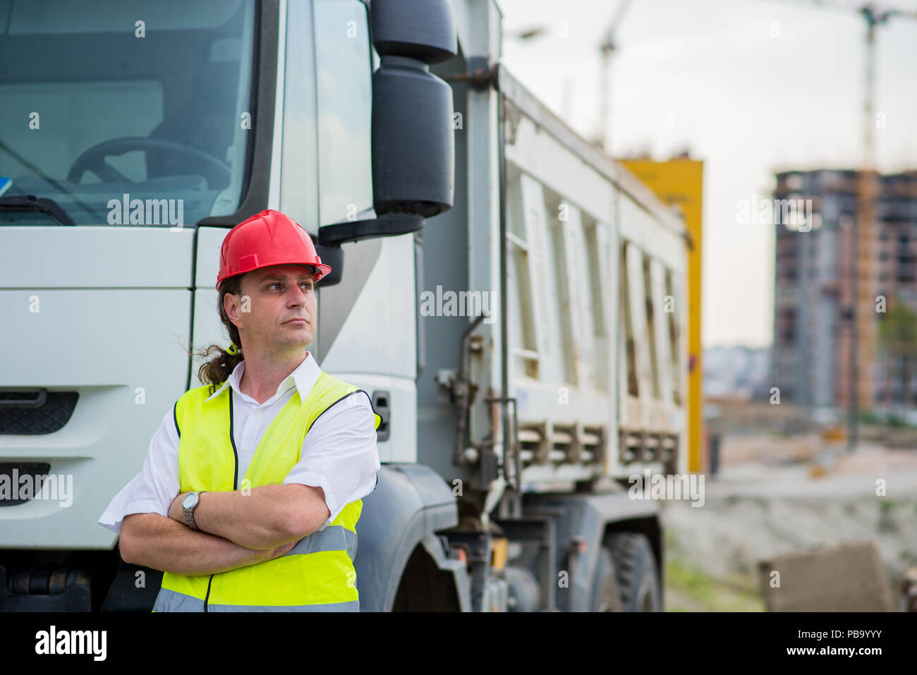 Lkw-Fahrer vor einem Lkw auf einer Baustelle mit verschränkten Armen Stockfoto