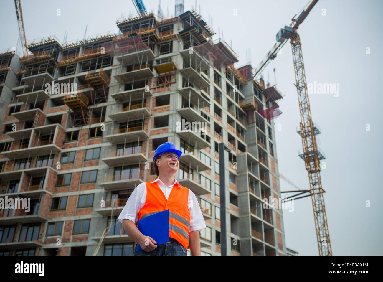 Lächelnd Ingenieur holding Dokumente auf einer Baustelle mit Gebäuden und Krane im Hintergrund Stockfoto