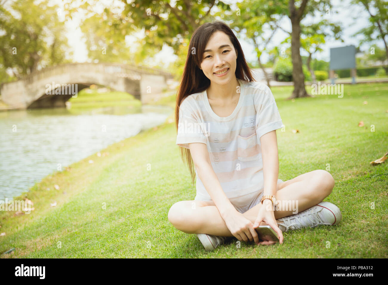 Asian teen Chinesische Rasse single Augenlid lange Haare sitzen Lächeln mit Grübchen Wange im Park Stockfoto