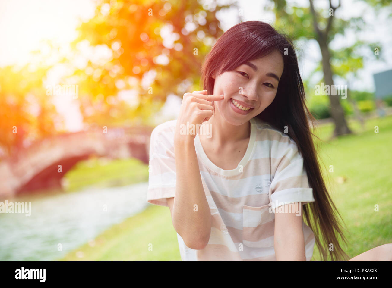 Süße asiatische Frau lächeln mit Finger Grübchen Wange im Park Stockfoto