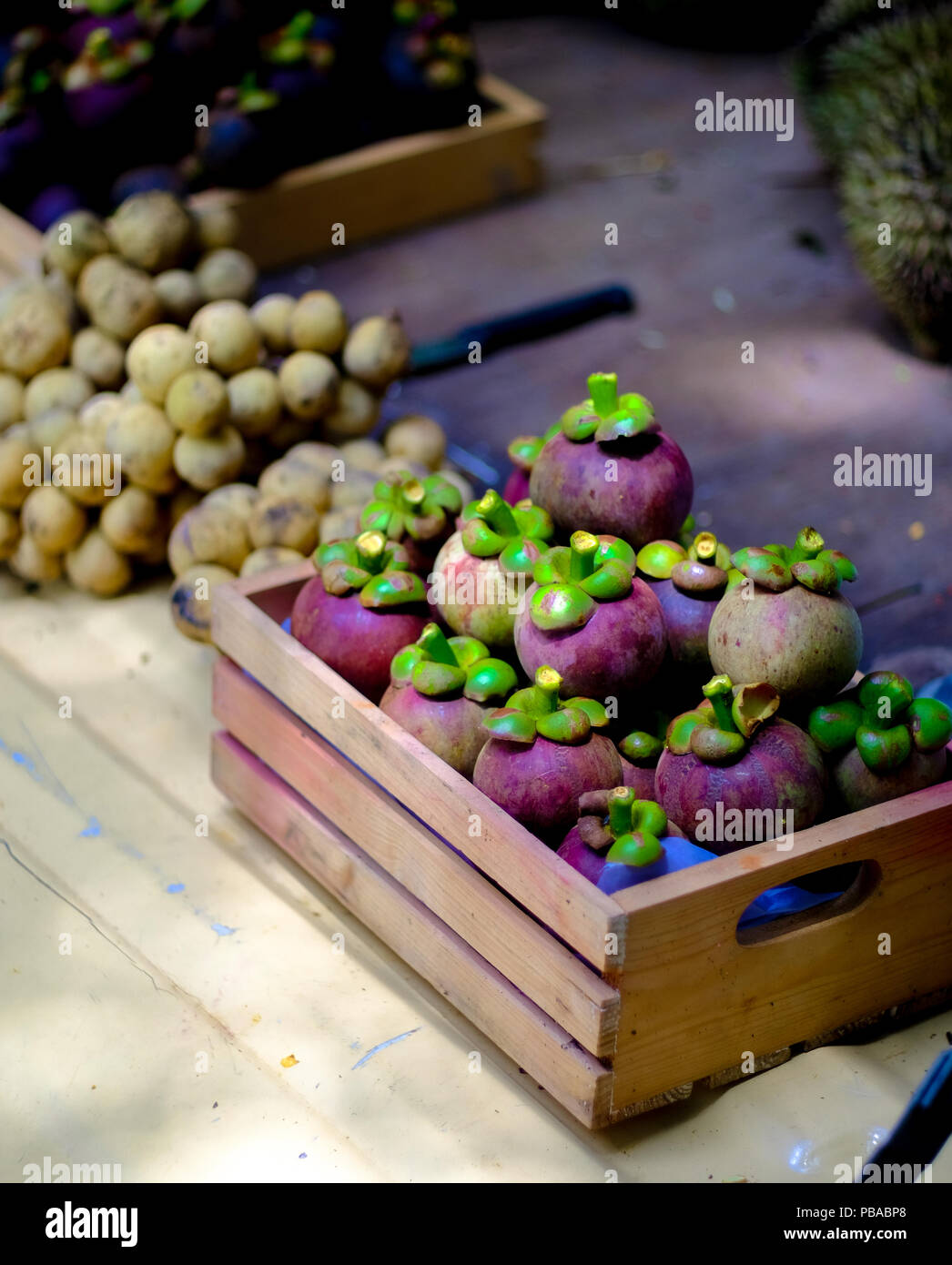 Der Stapel der Mangostan und wollongong sind in eine kleine Holzkiste. Auf einem hellen Gelb Oberfläche im Inneren der Markt im Freien, selektiven Fokus. Stockfoto