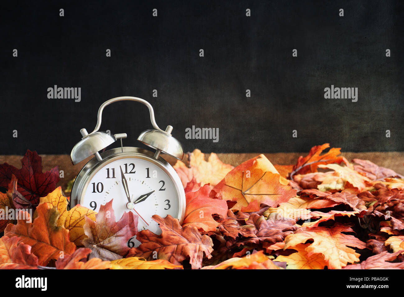 Wecker in bunten Blätter im Herbst gegen einen dunklen Hintergrund mit geringer Tiefenschärfe. Sommerzeit Konzept. Stockfoto