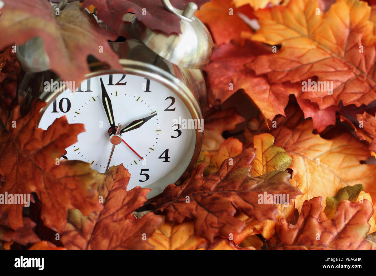 Vintage Wecker unter bunten gefallenen Blätter im Herbst mit einer geringen Tiefenschärfe begraben. Sommerzeit Konzept mit Uhr Hände an der Alm Stockfoto
