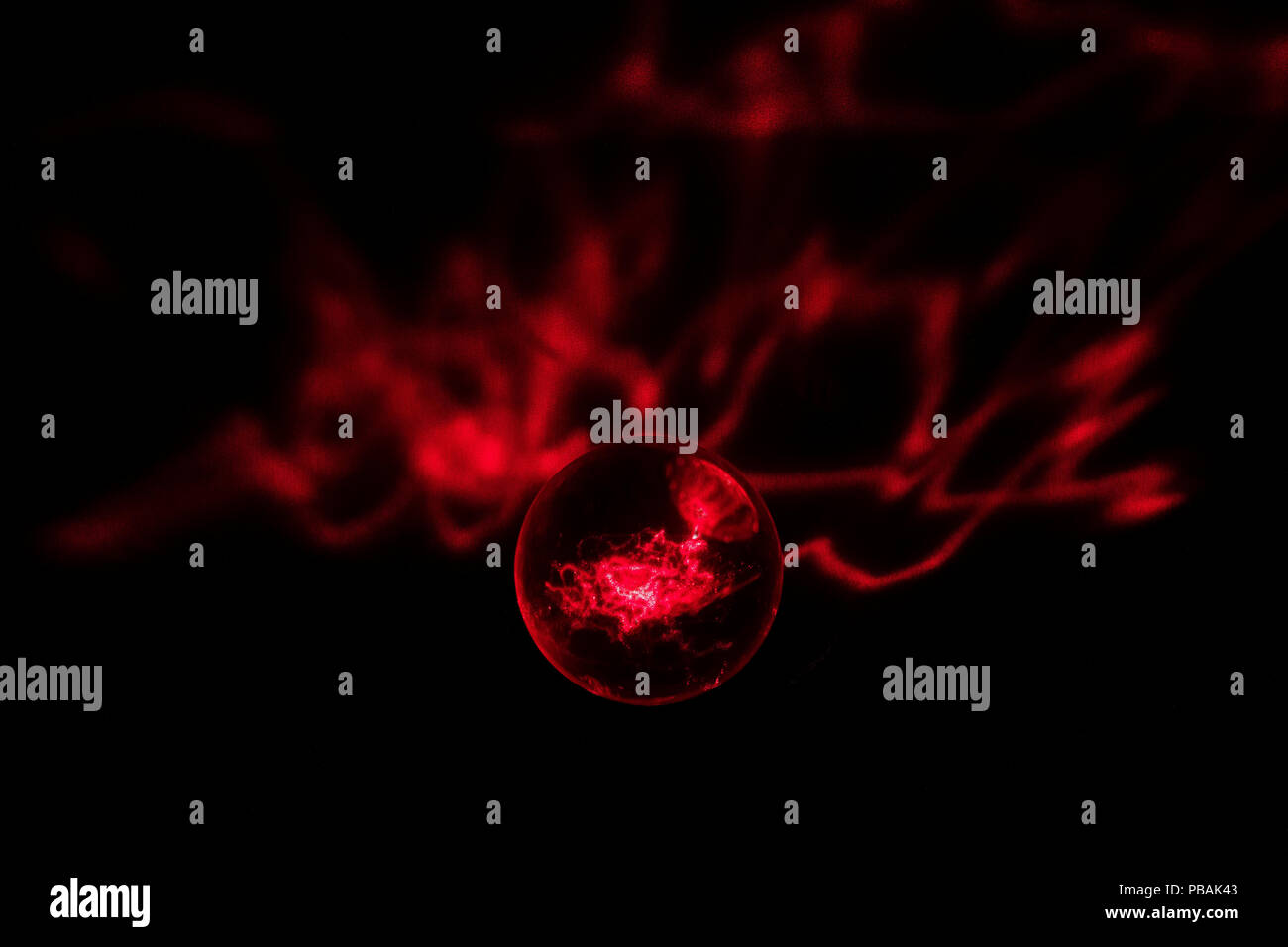 Ein roter Laserstrahl wird sowohl innerhalb als auch projizierte hinter einem Crystal Ball gefangen. Stockfoto