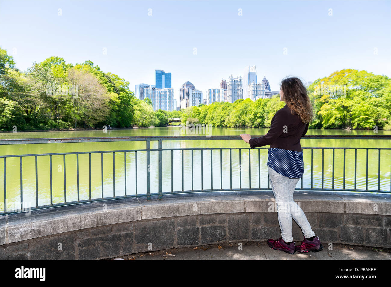 Eine junge Frau, die in Piedmont Park in Atlanta, Georgia am malerischen Blick, Wasser, Stadt, Skyline der Stadt Wolkenkratzer downtown, La Stockfoto