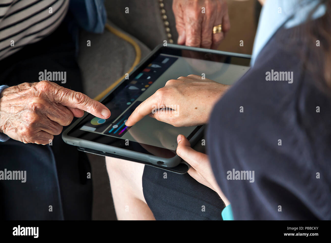 Junge Schulmädchen lehre es Fähigkeiten älterer Bürger auf Tablet über die Schulter pov Stockfoto