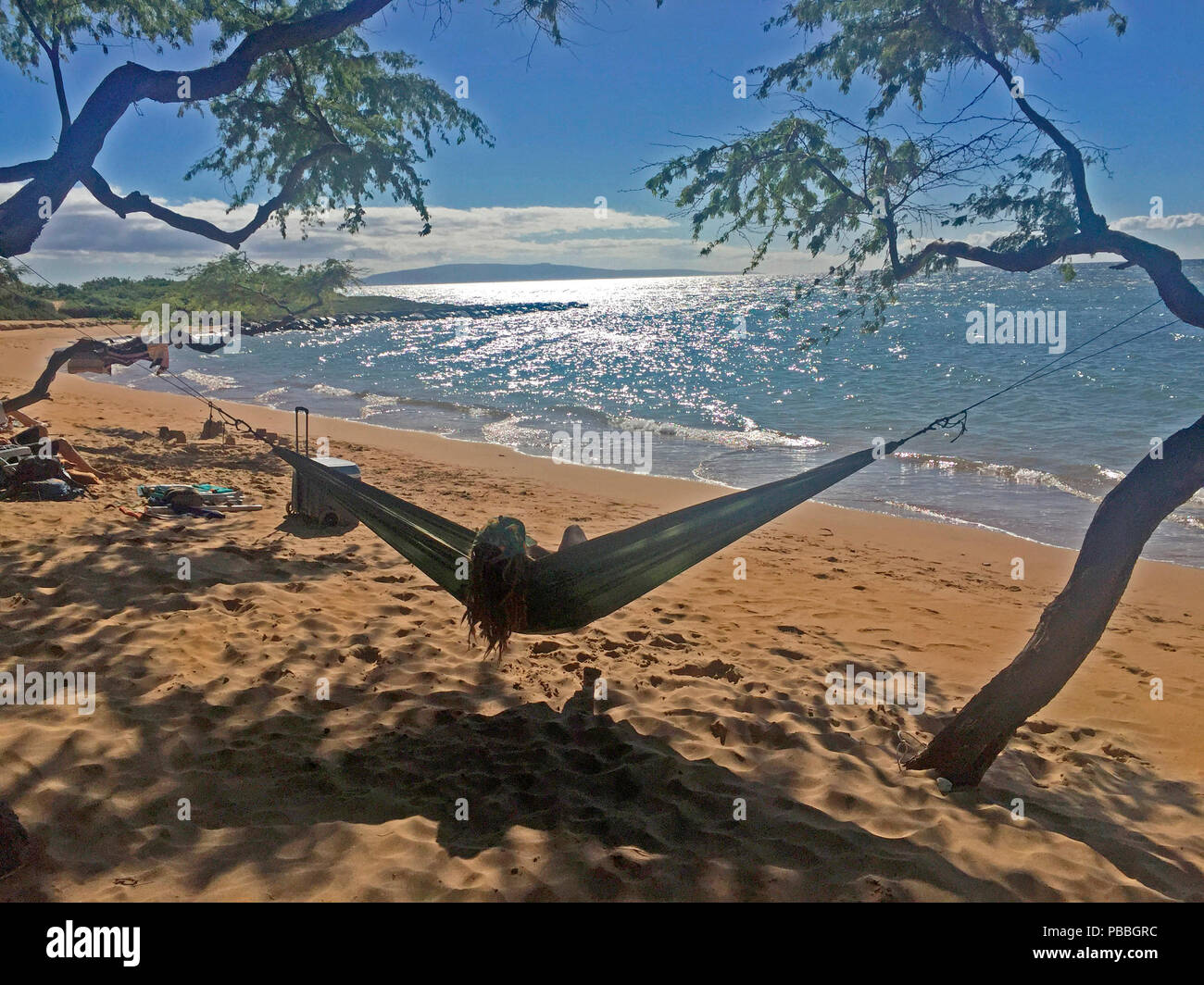 Eine Frau entspannt in der Hängematte am Strand im Schatten, Maui, Hawaii, USA. Die Weite des Pazifischen Ozeans erstreckt sich von Ecke zu Ecke. Stockfoto